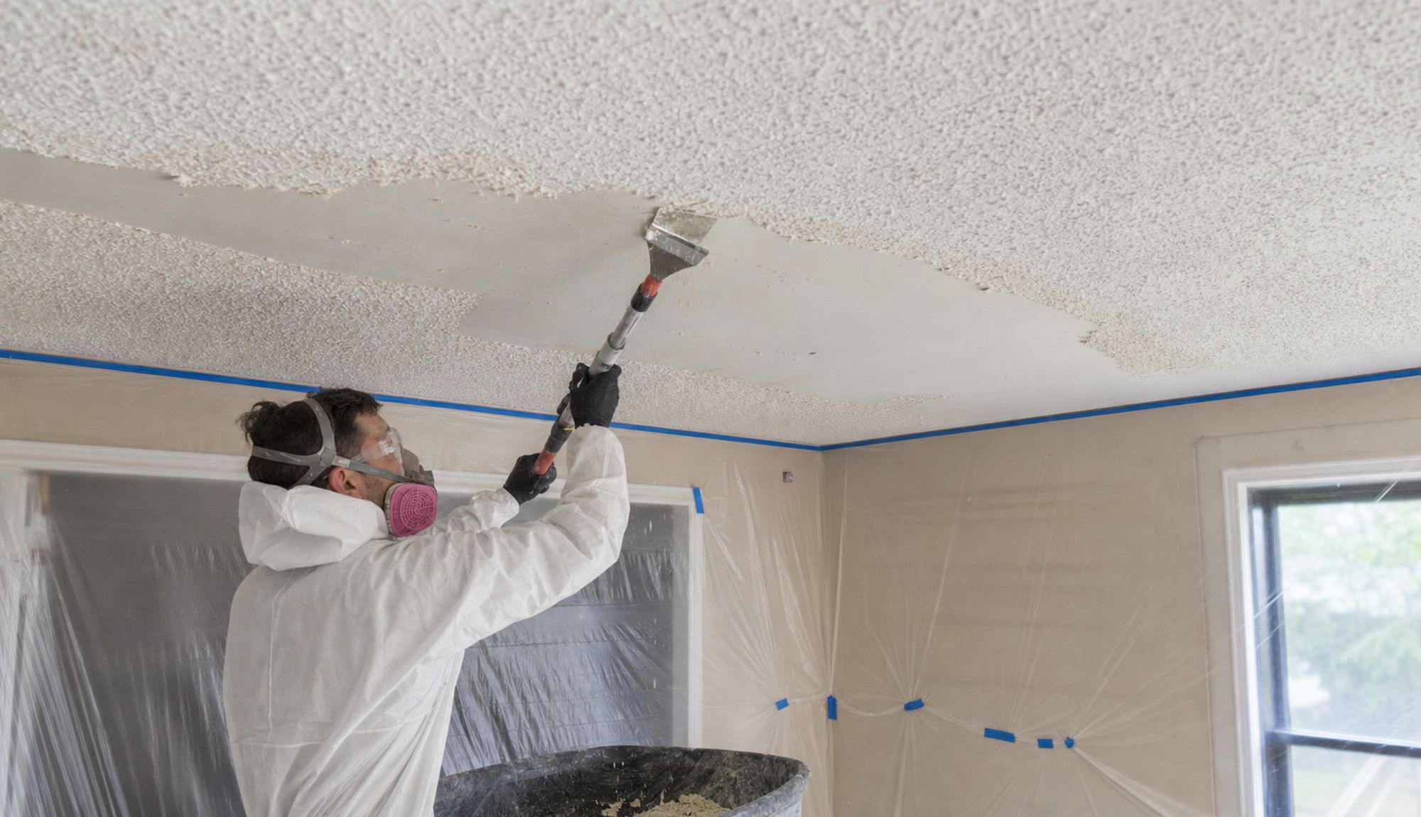 Worker scraping popcorn texture off a ceiling